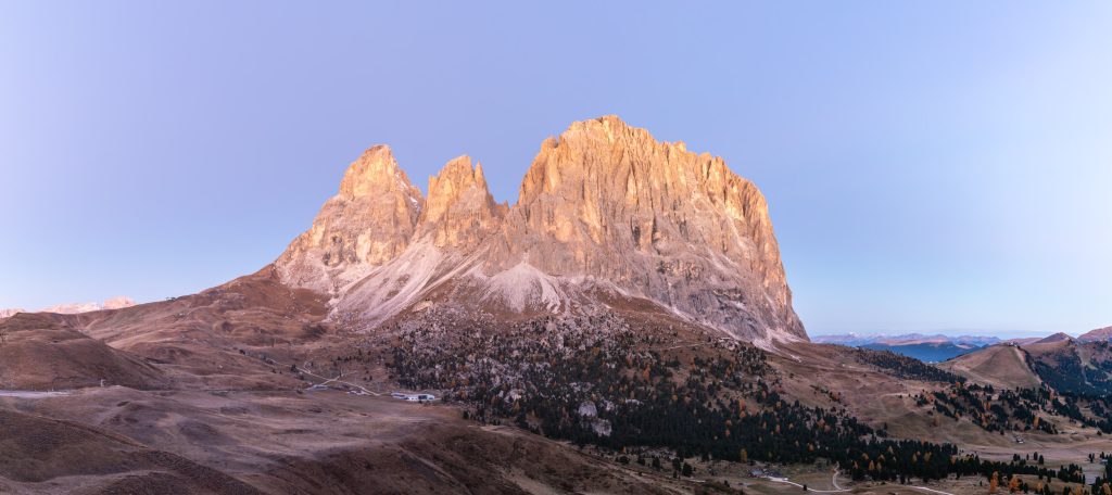 Panorama of the rising sun illuminating the craggy mountains of Sassolungo and Passo Gardena in the Dolomites of northern Italy.