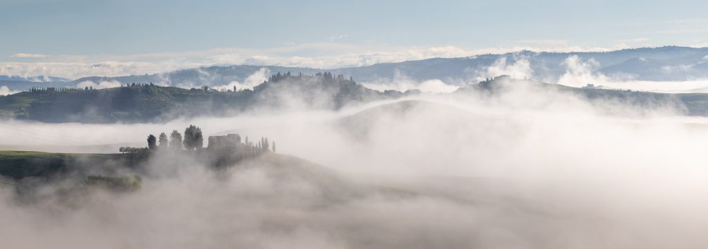 Panorama of the morning mist amongst houses on the Crete Senesi, Tuscany, Italy.