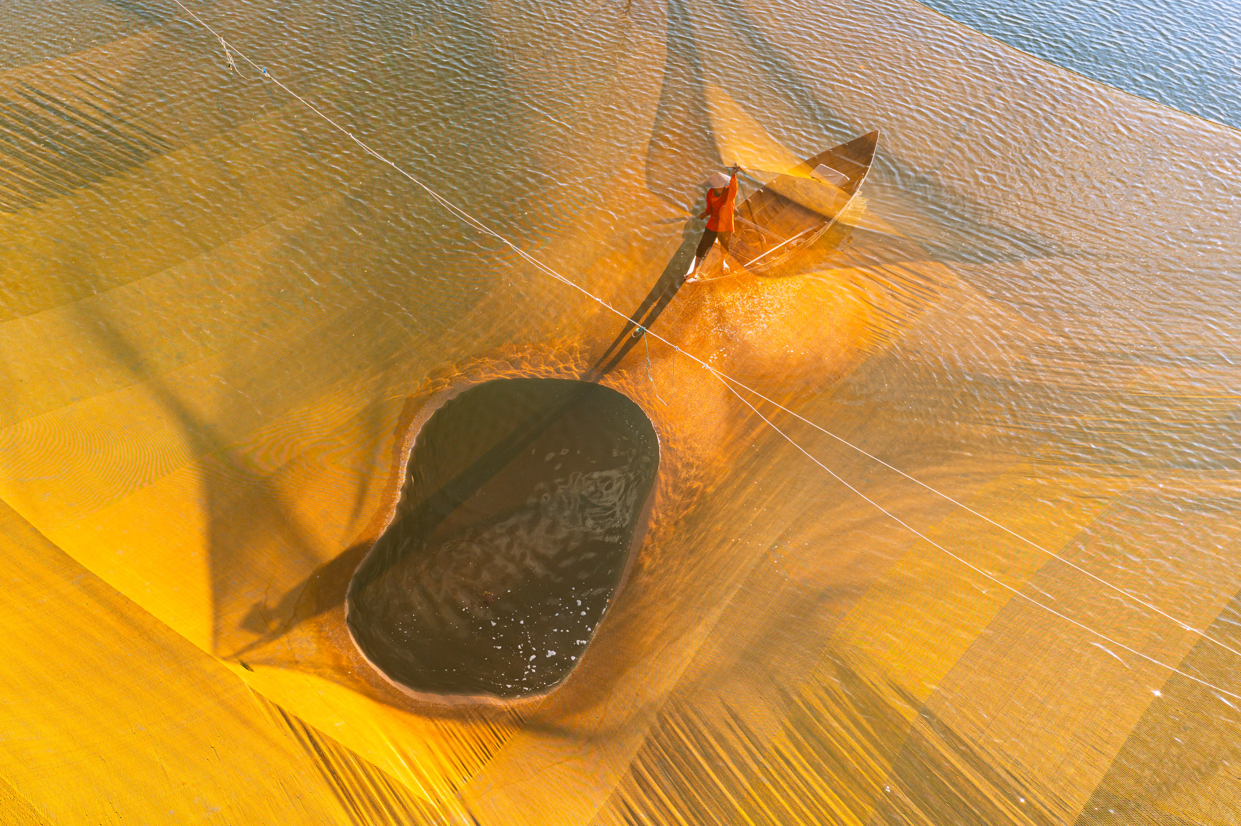 Aerial high-angle view of a fisherman at work during sunrise on the Thu Bon river near to Hoi An, Quang Nam, Vietnam.